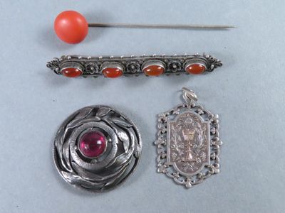une broche en argent, une épingle et une perle rouge posées sur une table