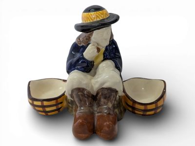 une figurine représentant un homme coiffé d'un chapeau et chaussé de bottes, assis sur un tonneau