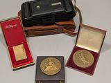 trois médailles d'or et un étui en cuir posés sur une surface blanche