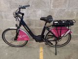 un vélo garé sur un parking, avec un sac rose à l'arrière