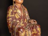 statue of a man sitting on a wooden floor with a black background