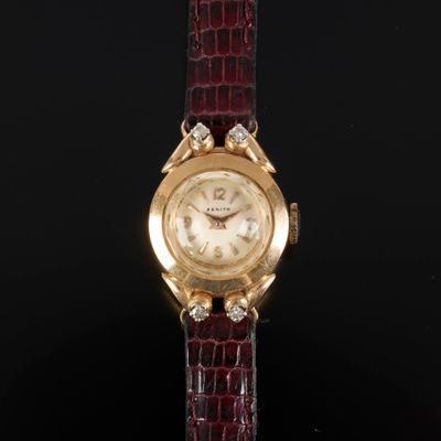 un gros plan d'une montre en or sertie de diamants, montée sur un bracelet rouge