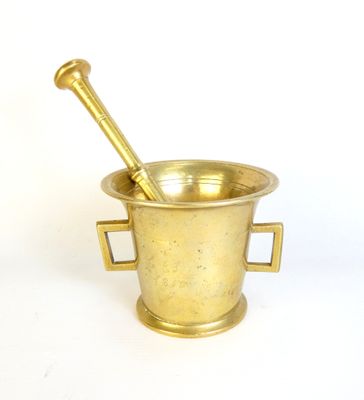 brass mortar and spoon on a white surface with a white background