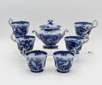 six tasses à thé bleues et blanches avec leurs soucoupes, posées sur un présentoir transparent