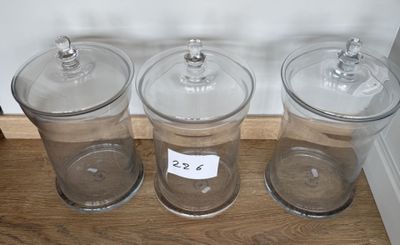 trois bocaux en verre transparent avec leurs couvercles sont posés sur une étagère en bois
