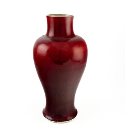 un vase rouge posé sur une surface blanche
