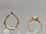 two gold rings with a pearl on top of a clear glass stand