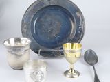 plusieurs objets en argent, dont une coupe, une cuillère et un repose-cuillère, posés sur une surface blanche