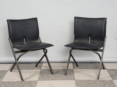 une paire de chaises pliantes en cuir noir adossées à un mur blanc, sur un sol à carreaux