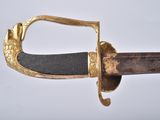 a close up of a sword on a white surface with a gold handle