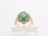 an emerald and diamond flower ring on a clear display stand