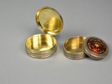 a small metal container with a lid that has a red substance inside of it