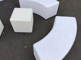 three white curved benches and two stools sitting on the ground
