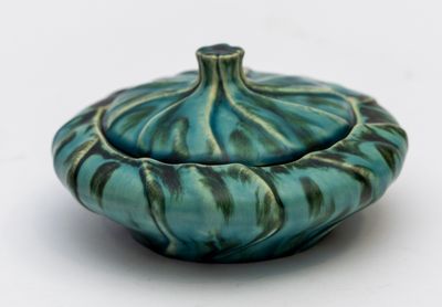 un bol bleu et vert avec un couvercle, posé sur une surface blanche