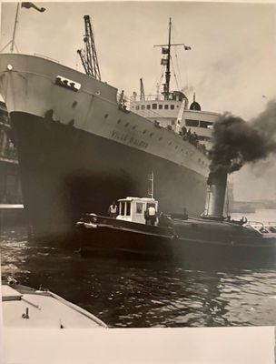 black and white photograph of a tugboat and a large ship in the water