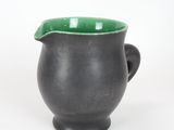 a black cup with a green handle on a white surface
