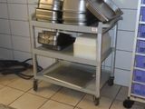 Plusieurs casseroles et poêles sont empilées sur un chariot métallique dans une cuisine.