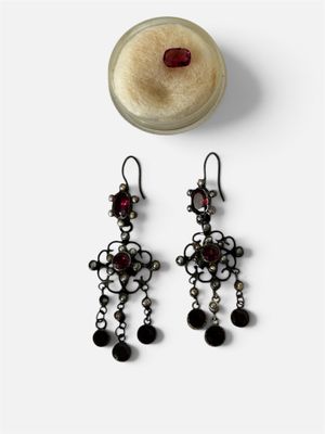 une paire de boucles d'oreilles noires et argentées ornées de grenats, accompagnée d'un bocal en verre
