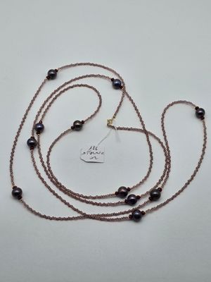 a close up of a long necklace with black beads on a white surface
