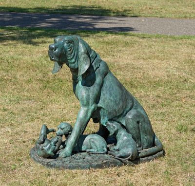 une statue représentant un chien avec une ribambelle de bébés dans l'herbe