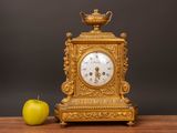 a gold clock sitting on a table next to an apple