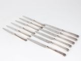 six knives are lined up on a white surface