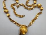 un collier en or orné d'une boule et d'une chaîne, posé sur un fond blanc