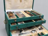 un coffret vert ouvert contenant de l'argenterie, posé sur une surface grise