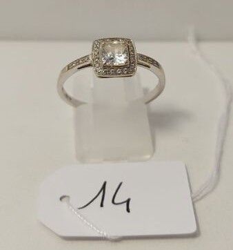 une bague en or blanc sertie d'un diamant taille carrée entouré d'un halo