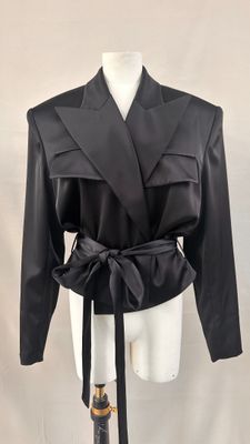 La veste est noire et comporte une ceinture à la taille.
