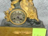 a gold clock with a woman sitting on top of it