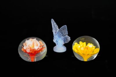 trois figurines en verre représentant des fleurs et un papillon sur fond noir
