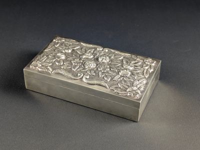 une boîte ancienne en argent, ornée de fleurs et de feuilles sur un fond noir