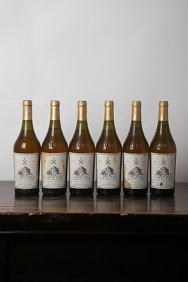 Six bouteilles de vin sont alignées sur une table devant un mur blanc.