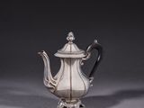 a silver teapot with a black handle on a gray surface