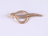 a gold brooch with a feather on it on a white surface