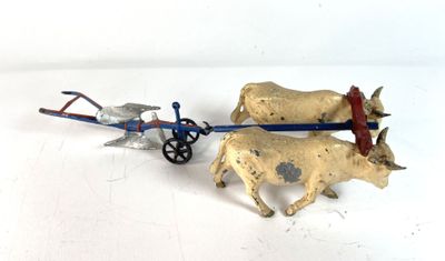 two figurines of cows pulling a cart on a white surface