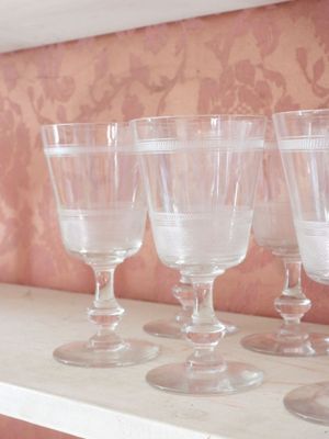 Plusieurs verres à vin vides sont alignés sur une étagère devant un mur recouvert de papier peint.