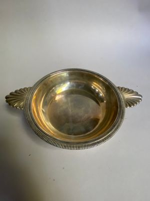 un plat ancien en argent posé sur une table blanche, muni d'une poignée en argent