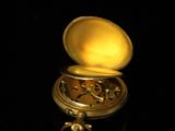 a small gold pocket watch sitting on a black surface
