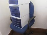 des cartons empilés sur une chaise de bureau bleue, dans un coin