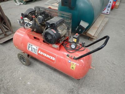 a red air compressor sitting on the ground next to a blue tank