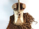 un masque en bois posé sur un morceau de tissu, lui-même posé sur une surface blanche