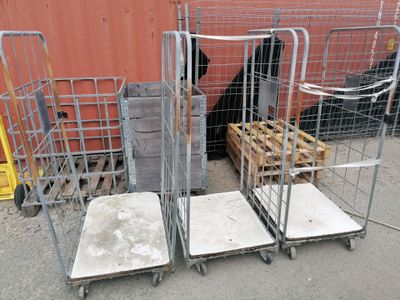 plusieurs chariots métalliques chargés de matelas et de caisses devant un bâtiment rouge