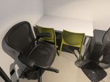 a desk with two chairs and a fan in the corner