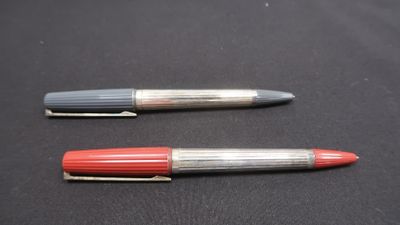 two pens sitting on top of a black surface next to each other