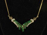 a gold necklace with green and white stones on a black mannequin