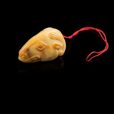 un petit morceau représentant une tête d'animal sculptée, suspendu à un cordon rouge