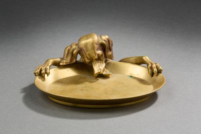 une assiette en or sur laquelle est représenté un chien, posée sur un fond gris