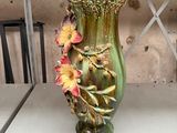 a green vase with flowers on it sitting on a shelf